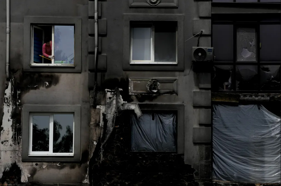 یک زن خانه دار اوکراینی در شهر "بوچا" در حال تمیز کردن شیشه پنجره خانه اش 