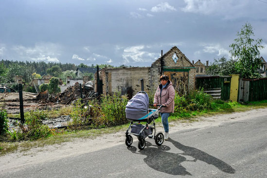عبور مادر اوکراینی از کنار ویرانه های برجای مانده از جنگ