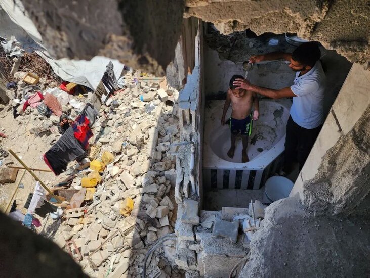 پدری در حال حمام کردن فرزندش در خانه ویران شده