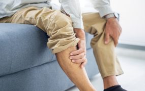 Old,Man,Suffering,From,Knee,Pain,Sitting,Sofa,In,The